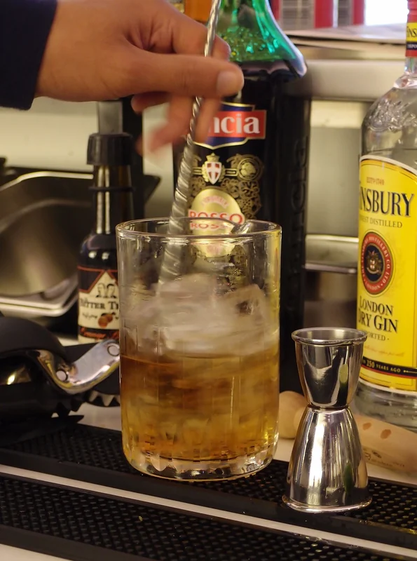 A cocktail being stirred with a bar spoon in a mixing glass
