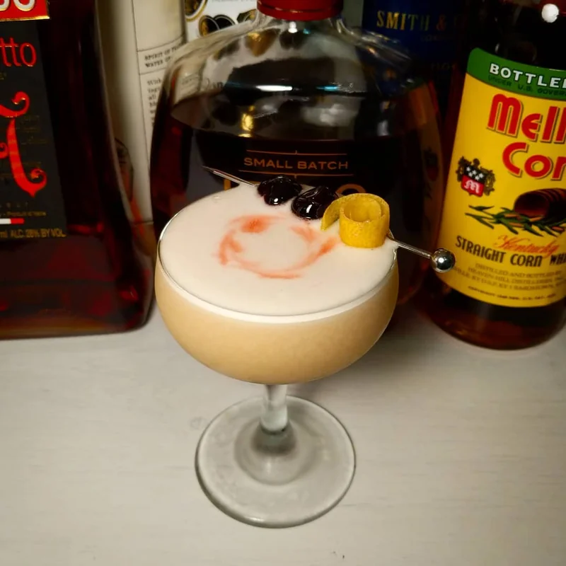 A Whiskey Sour in a coupe glass with cherry and orange garnish