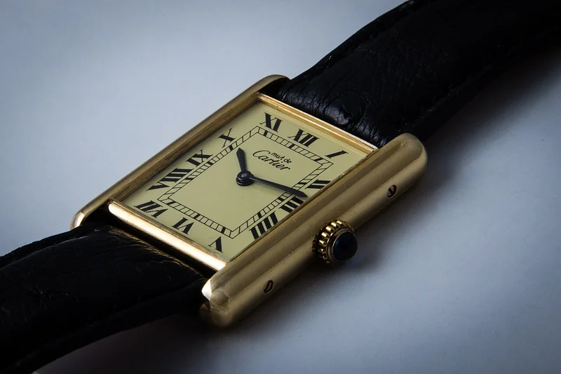 Cartier Tank rectangular watch with Roman numeral white dial, blue steel hands, and leather strap