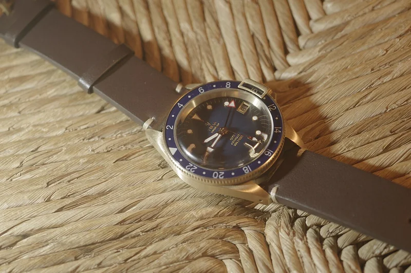 GMT watch dial showing 12-hour hands and 24-hour fourth hand against a rotating two-tone bezel